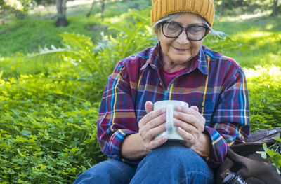 Senior woman holding coffee cup sitting outdoors