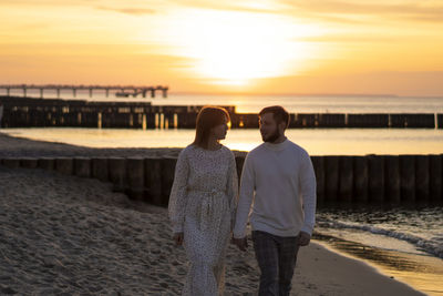 Rear view of couple standing on beach during sunset