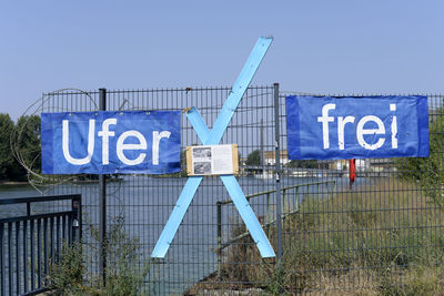 Information sign by fence against blue sky