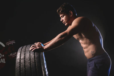 Side view of young man holding wheel against black background