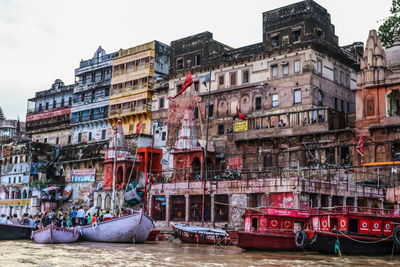 Boats moored in canal by buildings against sky in city