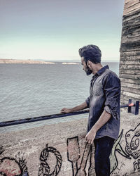 Side view of young man standing by sea against sky