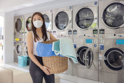 In the self-service laundry with dryer machines in the backdrop, a young woman enjoys clean ironed.