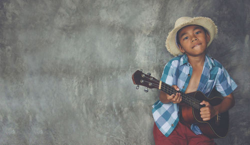 Portrait of boy playing guitar against wall