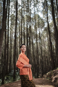 Portrait of woman standing by tree trunk in forest