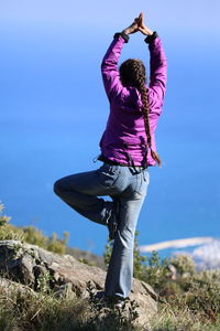 Rear view of woman doing yoga on field against clear sky