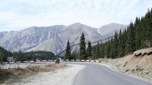 Road amidst trees and mountains against sky