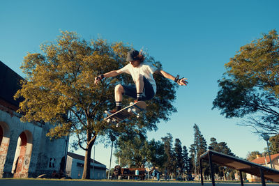 Low angle view of young woman jumping against clear sky