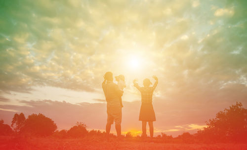 Rear view of friends standing against sky during sunset