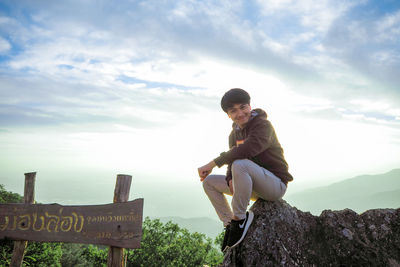 Portrait of man sitting on rock against sky