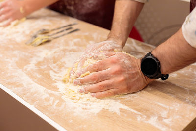 The hands of several people are kneading the dough on the table. mix a raw egg with flour.