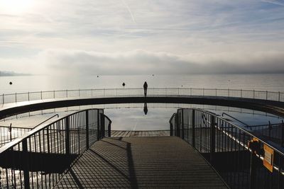 Man standing on staircase by sea against sky