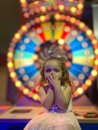 Portrait of girl sitting against illuminated game