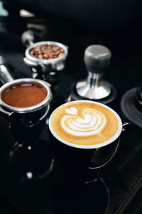 A portafilter with coffee beans, a portafilter with ground coffee, an empty cup of hot cappuccino