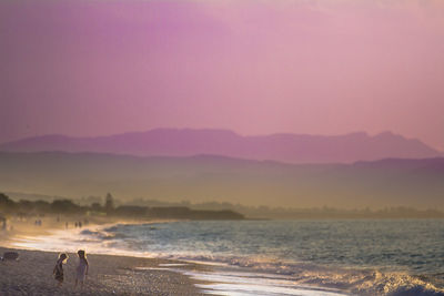 Children playing at beach against purple sky on sunny day