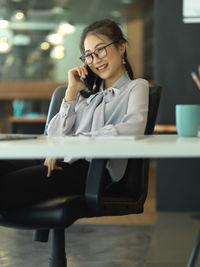 Woman talking over phone while sitting in office