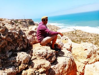 Side view portrait of man sitting on rock at beach