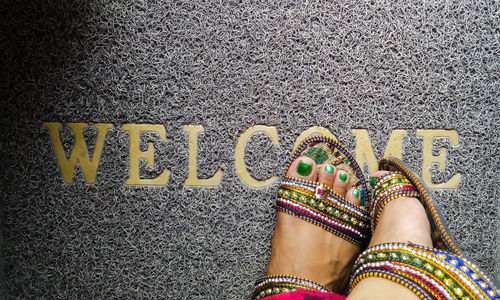 Low section of woman standing on door mat with text