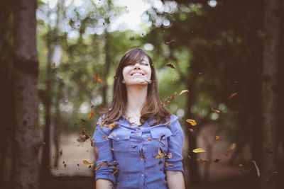 Happy young woman with eyes closed standing in forest during autumn