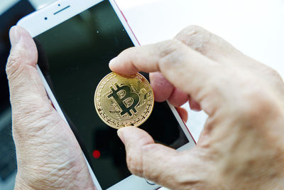 Close-up of hand holding bitcoin on smart phone screen