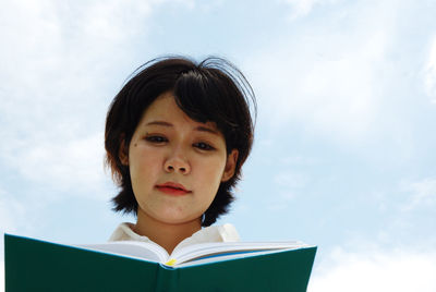 Low angle view of woman reading diary against sky
