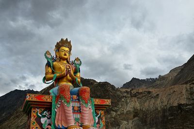 Low angle view of large maitreya buddha statue by rocky mountains against cloudy sky