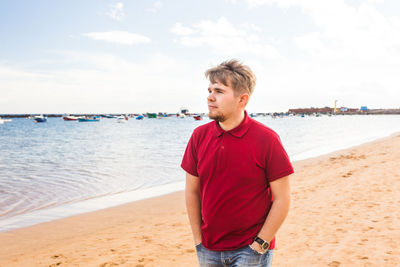 Young man standing on beach against sky