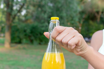 Beautiful woman is opening a bottle of fresh cold juice on the bench in the park in hot summer day