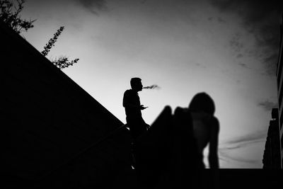 Low angle view of silhouette man smoking while standing against sky