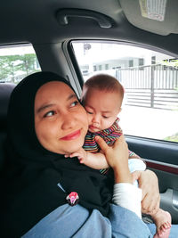 Muslim mother holding little baby daughter. asian wearing head scarf, sitting in the car with baby.