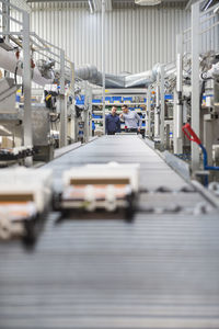Two men talking at conveyor belt in factory shop floor
