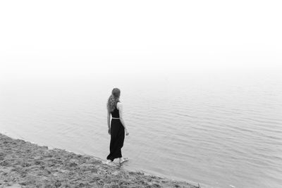 Rear view of woman standing on beach against clear sky