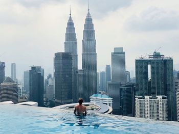 Woman swimming in infinity pool against modern buildings in city