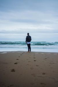 Rear view of man standing on beach against sky