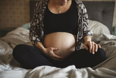 Pregnant woman sitting on bed and touching belly