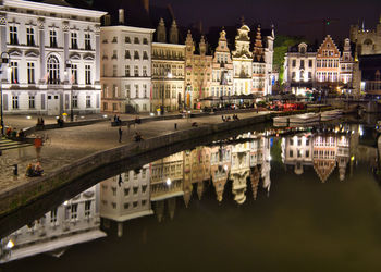 Bridge over river by buildings in city at night