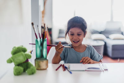 Little girl sitting at table and painting pictures of animals.