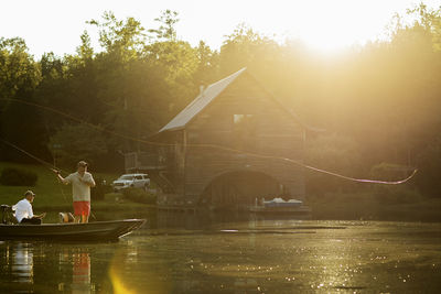 Man casting fishing line in lake with friend in rowboat