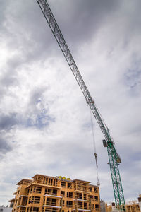 Low angle view of crane by building against sky