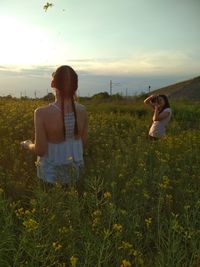 Friends standing amidst flowering plants on field against sky