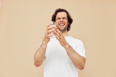 Smiling man holding water glass against beige background