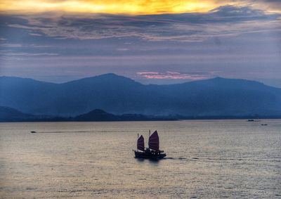 Sailboat in sea against mountains during sunset