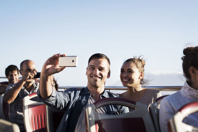 Couple taking selfie while traveling in double-decker bus against clear sky