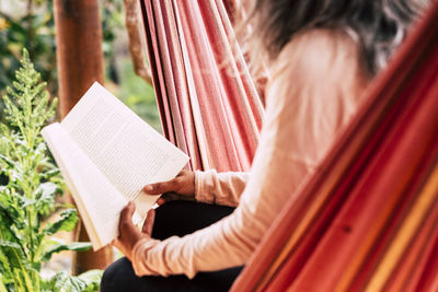 Midsection of woman reading book while sitting on hammock