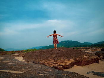 Rear view of boy standing on rock against sky