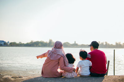Rear view of people sitting on shore against clear sky