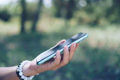 Cropped image of hand holding mobile phone outdoors