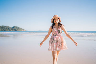 Full length portrait of young woman on beach against sky