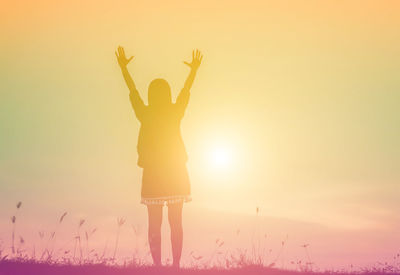 Rear view of woman standing on field against sky during sunset