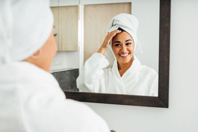 Smiling young woman looking at mirror in bathroom